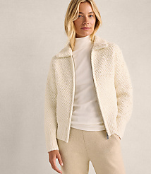 A blonde woman wearing a white textured zip-up jacket and beige trousers stands against a plain, light-colored wall. carousel Product Image 5