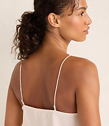 A woman with curly brown hair tied back wearing a white slip dress stands against a plain, light-colored background. carousel Product Image 3
