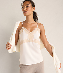 A woman wearing a white lace-trimmed camisole and a white cardigan draped over her shoulders stands against a plain, neutral-toned wall. carousel Product Image 1