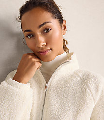 A woman wearing a white fleece jacket and turtleneck poses against a neutral, textured wall. carousel Product Image 2