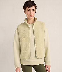 A woman with short dark hair wears a cream-colored fleece vest over a matching sweatshirt and olive green leggings against a plain, neutral background. carousel Product Image 1