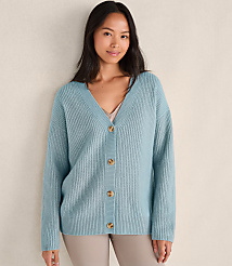 A woman wearing a light blue ribbed cardigan and beige pants stands against a plain, neutral-toned wall. carousel Product Image 1