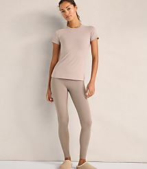 A woman wearing a beige short-sleeved t-shirt and matching leggings stands against a plain, light-colored wall. carousel Product Image 1