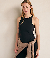 A woman wearing a black tank top and leggings with a tan sweater tied around her waist stands against a plain, light-colored wall. carousel Product Image 1
