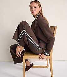 A woman wearing a brown tracksuit and loafers sits on a wooden chair against a plain, light-colored wall. carousel Product Image 4