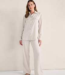A woman wearing a cream-colored button-down shirt and matching wide-leg trousers stands against a plain, neutral-toned wall. carousel Product Image 1