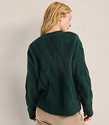 A woman with blonde hair wearing a dark green cable-knit sweater and tan pants stands against a plain, light-colored wall. carousel Product Image 2