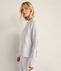 A blonde woman wearing a light-colored cable-knit sweater and matching pants stands against a plain, neutral-toned wall. carousel Product Image 2