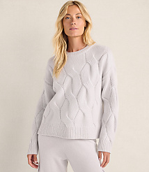 A blonde woman wearing a light purple cable-knit sweater and matching pants stands against a plain, neutral-colored wall. carousel Product Image 1