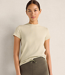 A woman wearing a light-colored ribbed t-shirt and olive green leggings stands against a plain, neutral-toned wall. carousel Product Image 1