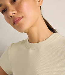 A close-up of a woman with freckles wearing a beige ribbed t-shirt against a plain, light-colored wall. carousel Product Image 2