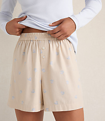A person wears a light blue long-sleeved shirt and beige patterned shorts against a neutral, textured background. carousel Product Image 2