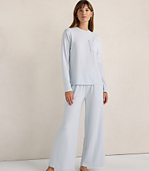 A woman wearing a light blue long-sleeved top and wide-leg pants stands against a plain, neutral-toned wall. carousel Product Image 2
