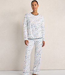 A woman wearing white and blue patterned pajamas stands against a plain, light-colored wall. carousel Product Image 2