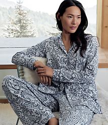 A woman wearing grey and white paisley pajamas sits on a chair in the foreground, with a snowy forest landscape visible through a window in the background. carousel Product Image 5