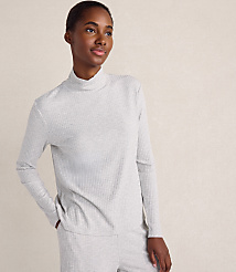 A woman wearing a light grey ribbed turtleneck and matching pants stands against a plain, neutral-toned background. carousel Product Image 1