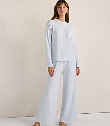 A woman wearing a light blue long-sleeved shirt and matching wide-leg pants stands against a plain, neutral-toned wall. carousel Product Image 1
