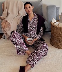 A woman in purple paisley pajamas sits on a white rug in the foreground, with a grey sofa and a woven basket in the background. carousel Product Image 5