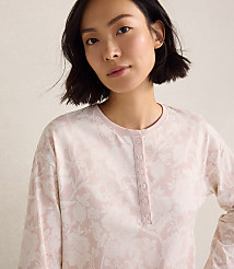 A woman with short dark hair wearing a light pink floral print top stands against a plain, neutral-colored background. carousel Product Image 3