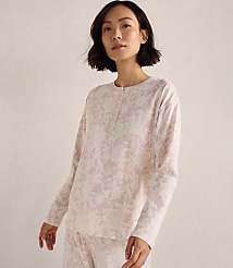 A woman wearing pink floral pajamas stands against a plain, neutral-toned background. carousel Product Image 1