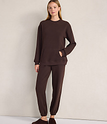 A woman wearing a brown lounge set and slippers stands against a plain, light-colored wall. carousel Product Image 1