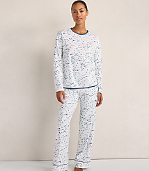 A woman wearing white and blue patterned pajamas stands against a plain, light-colored wall. carousel Product Image 1