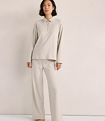 A woman wearing a light-colored, striped long-sleeved polo shirt and matching wide-leg pants stands against a plain, neutral-toned wall. carousel Product Image 1