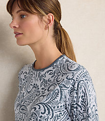 A woman with a ponytail wearing a blue and white paisley print shirt stands against a plain, light-colored wall. carousel Product Image 3