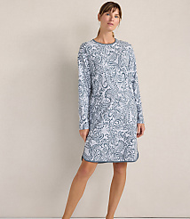 A woman wearing a blue and white paisley print long-sleeved dress stands against a plain, neutral-colored wall. carousel Product Image 1
