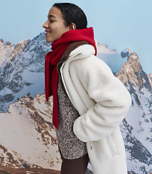 A woman wearing a white fleece jacket and a red scarf stands in profile against a backdrop of snowy mountains. carousel Product Image 5