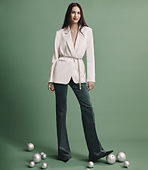 A woman wearing a white blazer and dark green trousers stands among silver ornaments against a solid green background. carousel Product Image 4