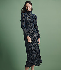 A smiling woman wearing a long-sleeved, dark teal patterned dress stands against a solid sage green background. carousel Product Image 4