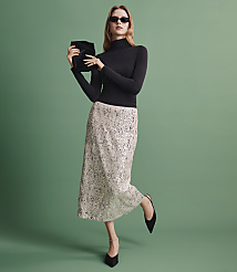 A woman wearing a black turtleneck, a shimmering silver sequined skirt, and sunglasses stands against a solid green background. carousel Product Image 5