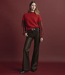 A woman wearing a red sweater and brown flared trousers stands against a solid red background. carousel Product Image 4
