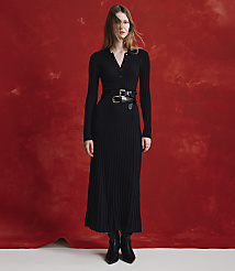 A woman wearing a long-sleeved black ribbed dress with a belt and black boots stands against a textured red background. carousel Product Image 4