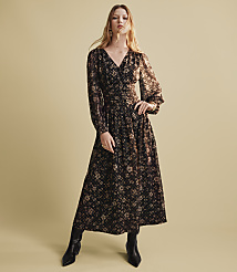 A woman wearing a long-sleeved floral maxi dress and black boots stands against a plain, light beige background. carousel Product Image 4