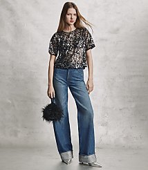 A woman wearing a sequined black top and wide-leg blue jeans stands against a textured grey wall. carousel Product Image 4