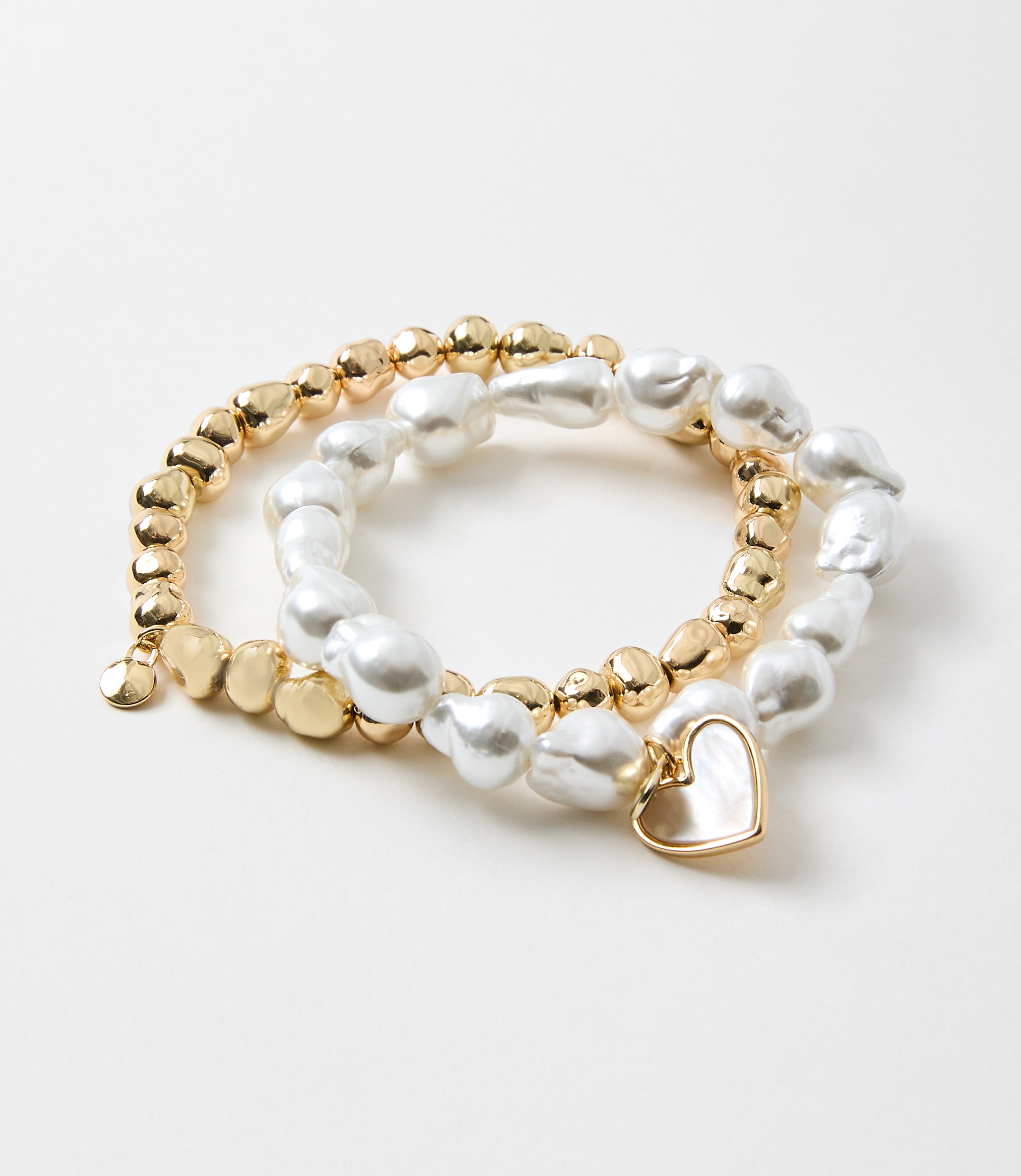 The image shows a set of three bracelets made of gold-colored beads and white irregular-shaped pearls, with a small heart-shaped charm attached to one of the bracelets.