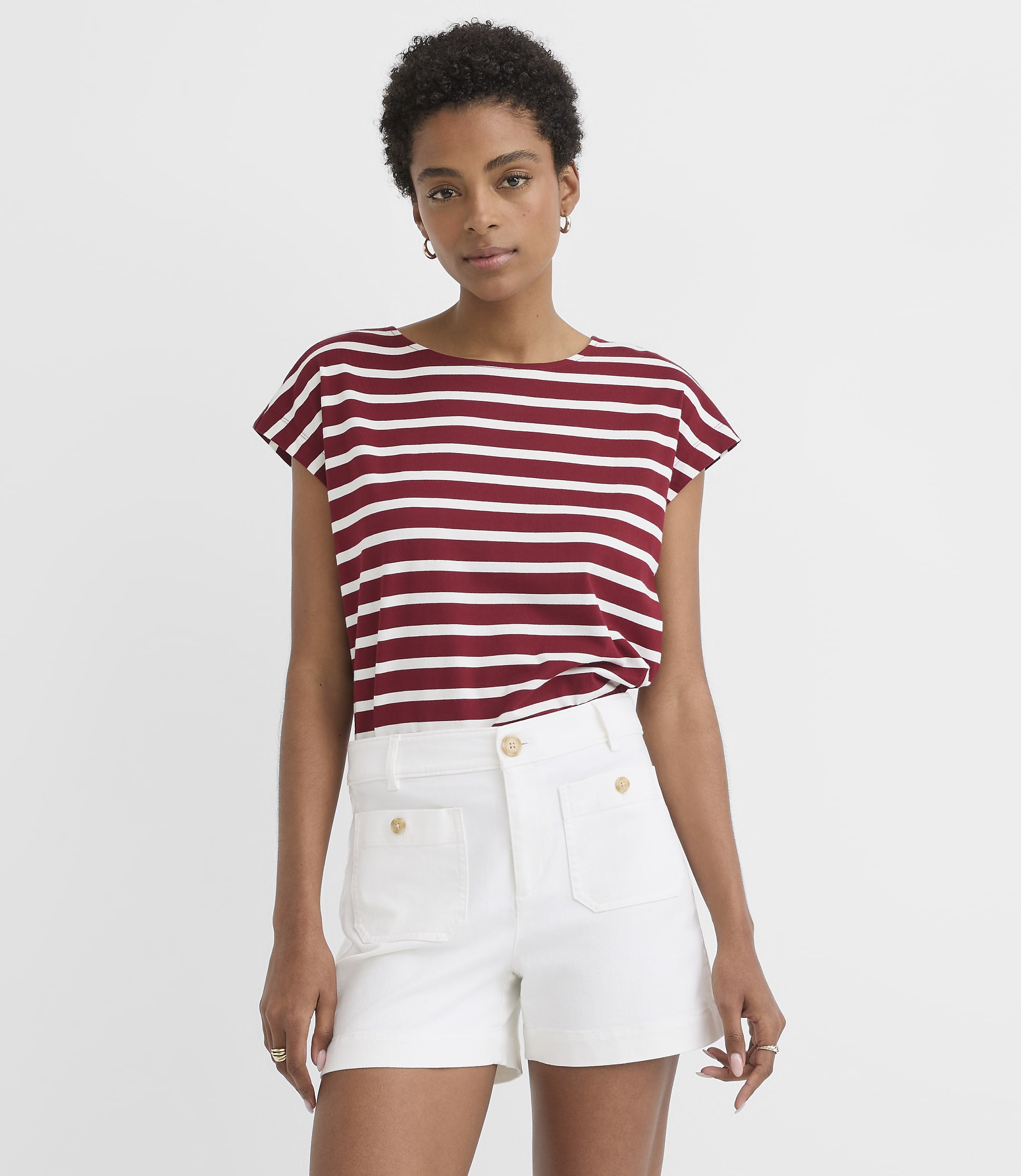 A woman in a striped t-shirt and white shorts stands against a plain white background.