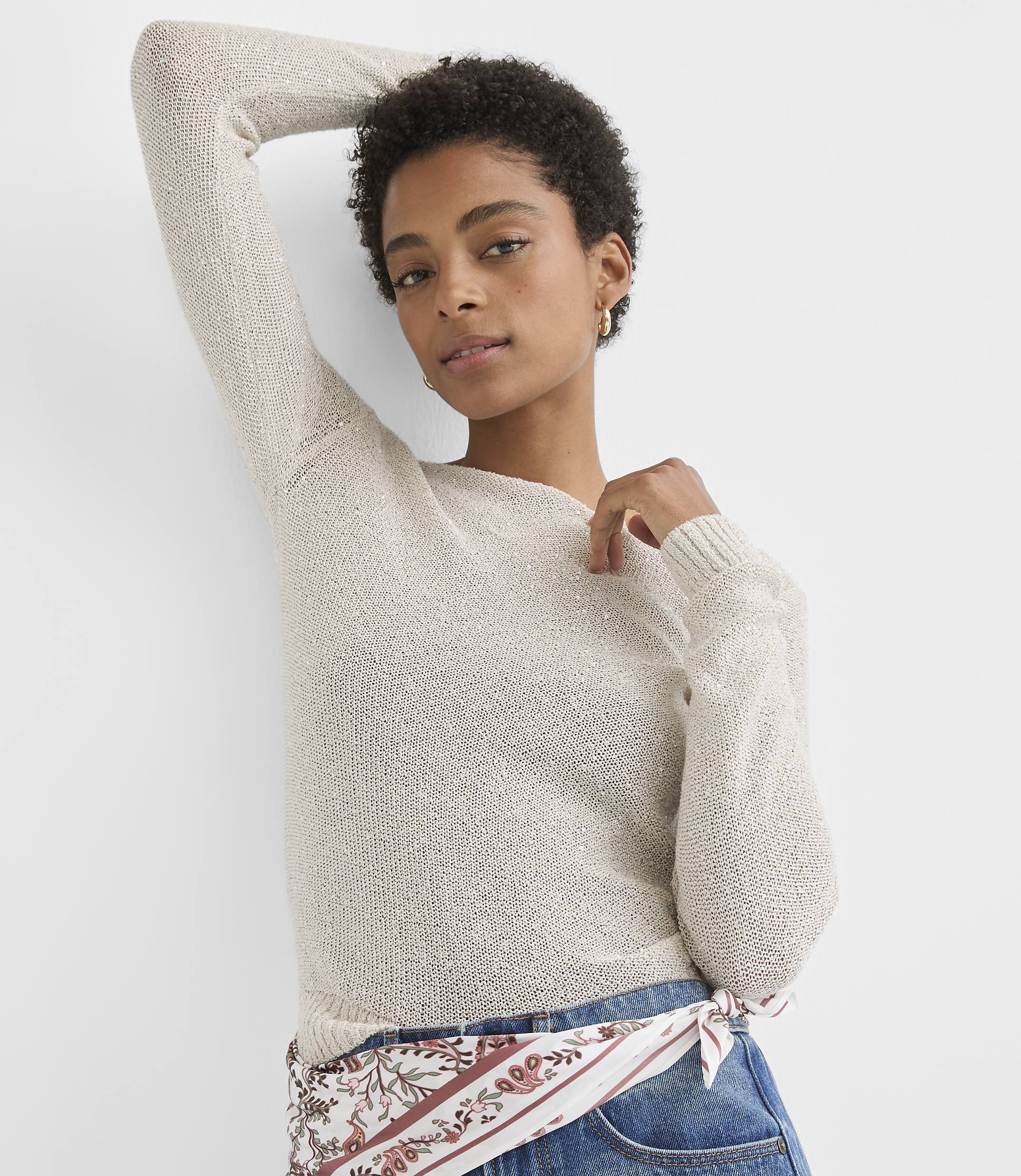 A woman in a light-colored sweater and jeans poses against a plain white background.