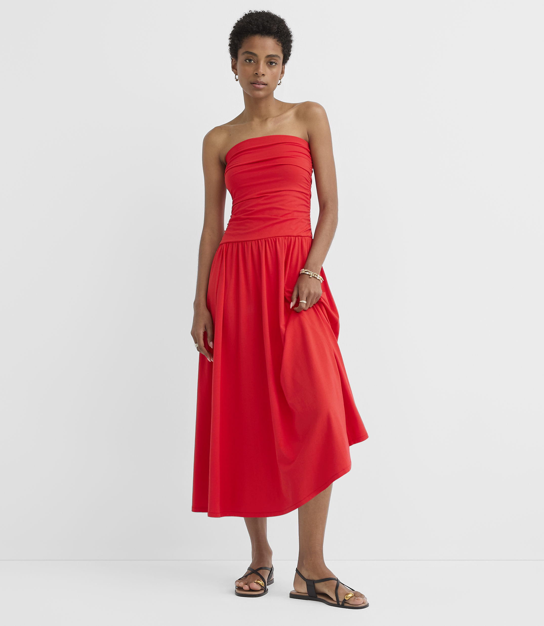 A woman in a red strapless dress stands against a plain white background.