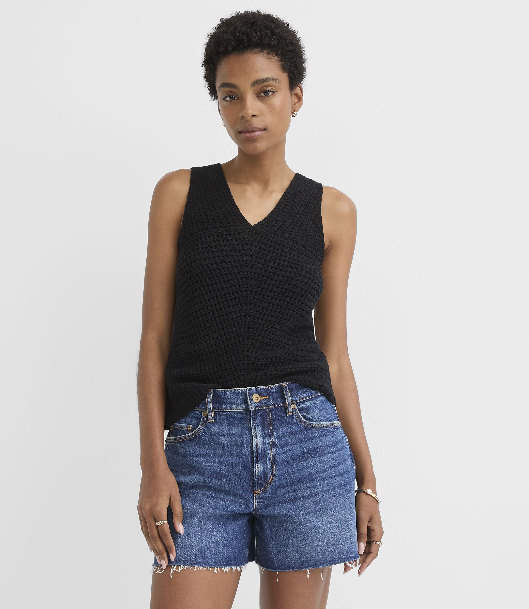 A woman in a black knit tank top and denim shorts stands against a plain white background.