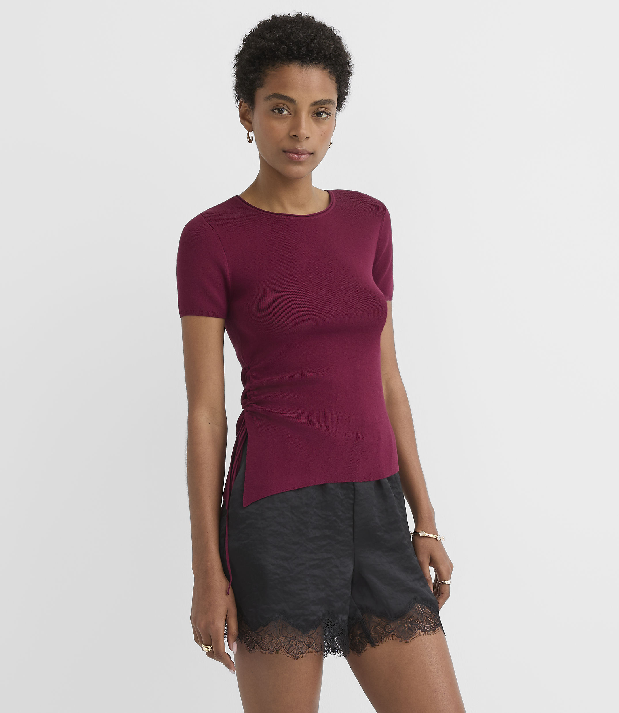 A woman in a maroon top and black lace-trimmed shorts stands against a plain white background.