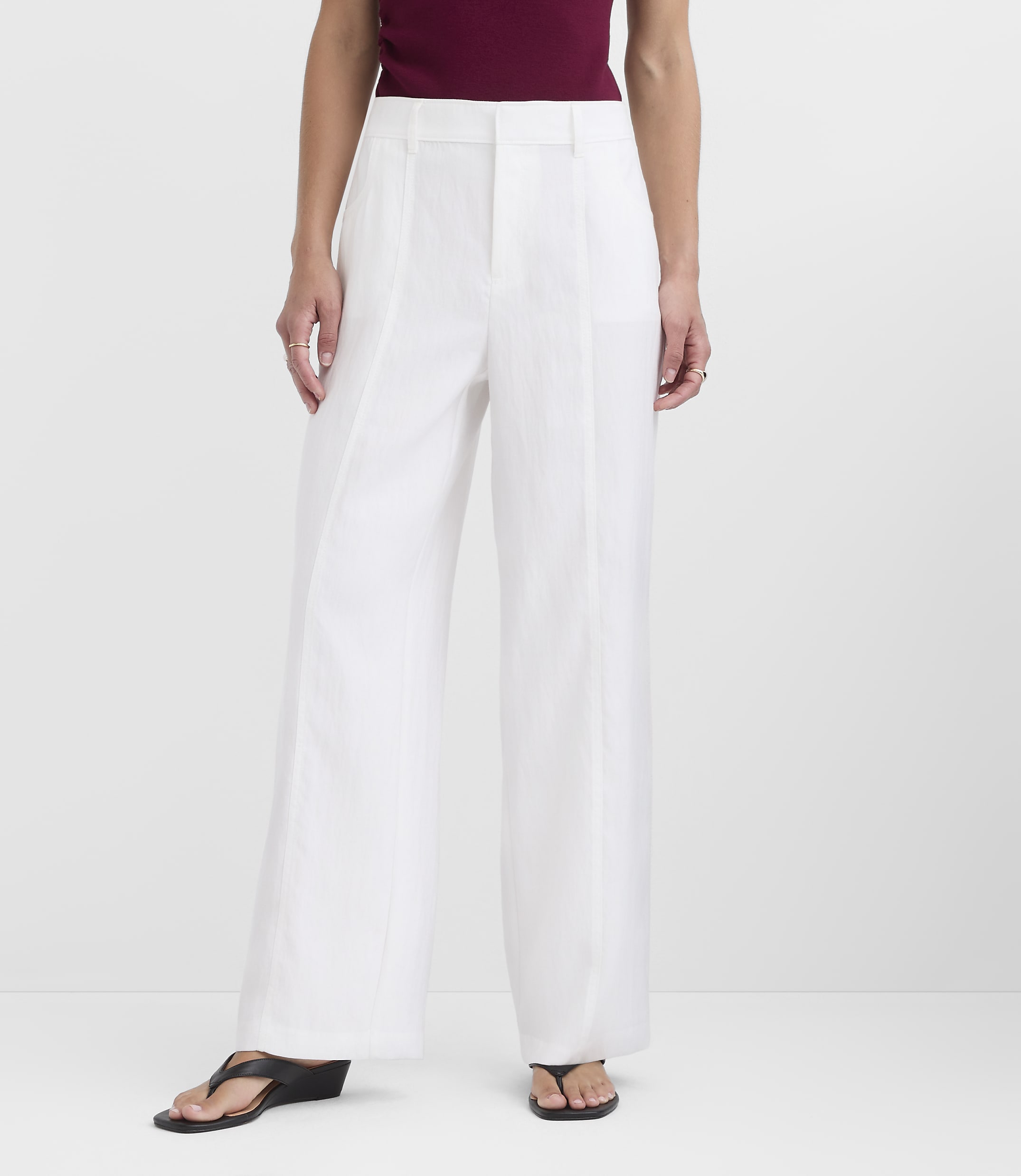 A person stands in white wide-leg pants and black sandals against a plain white background.