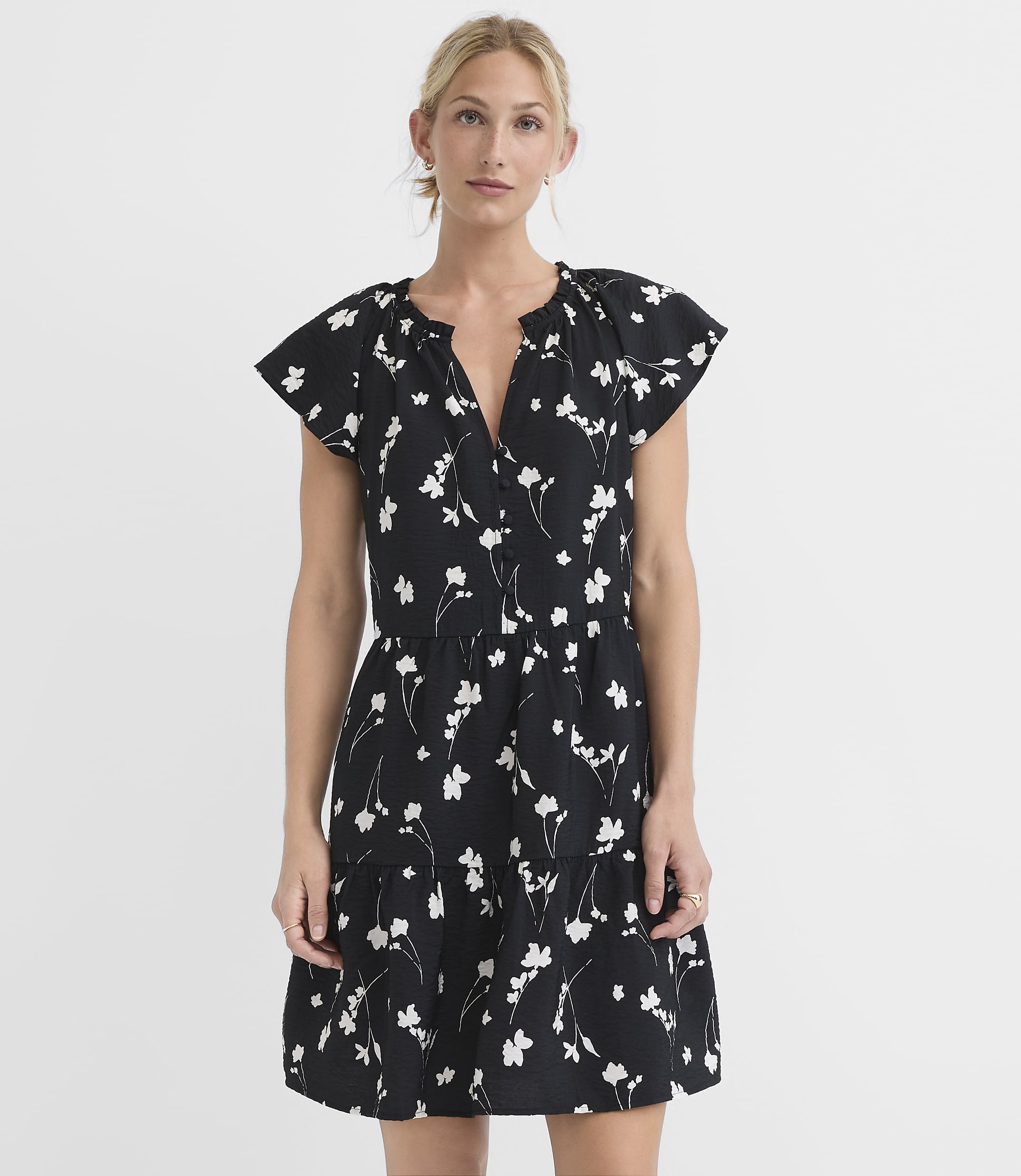 A woman in a black floral dress stands against a plain white background.