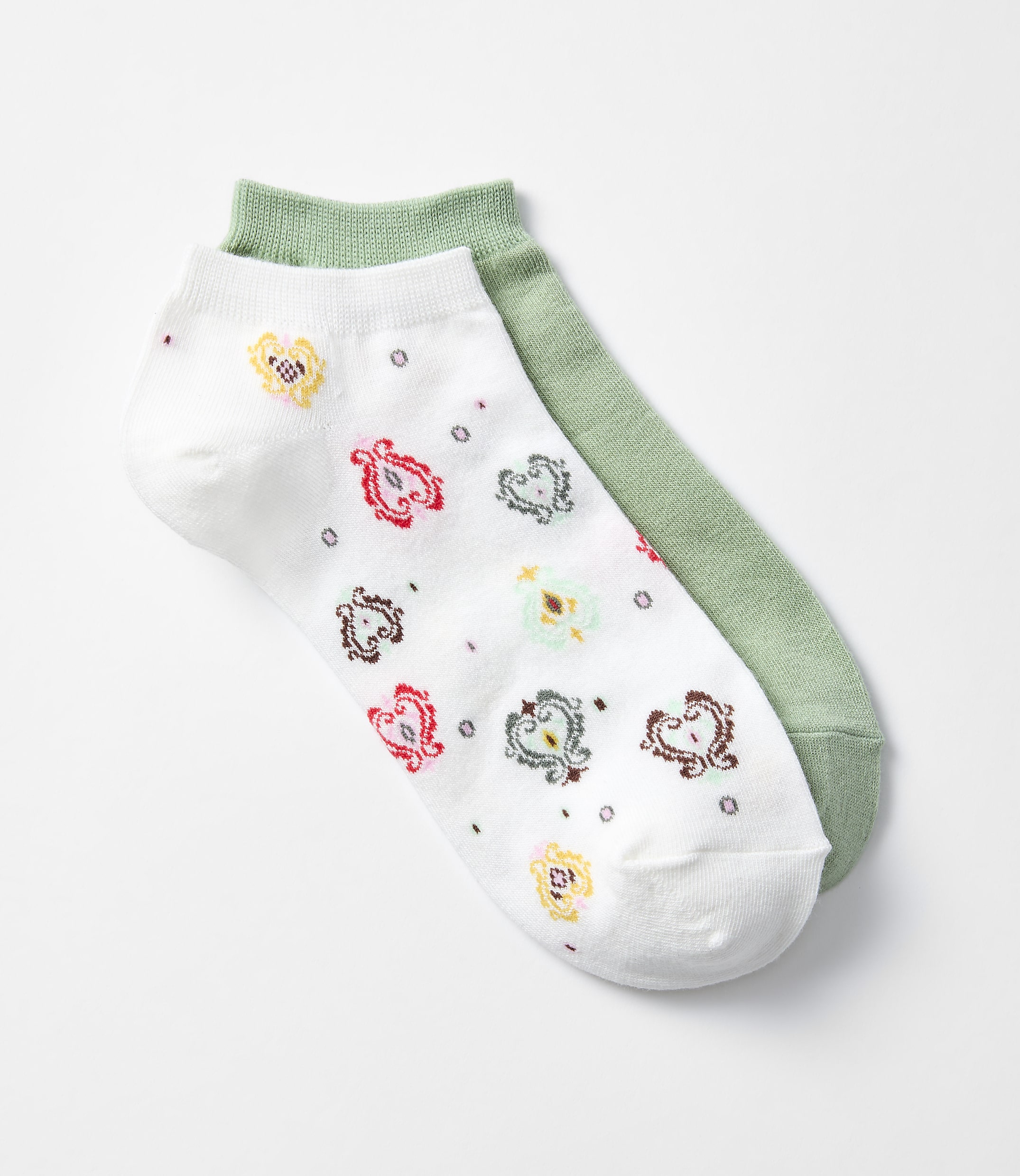 A pair of ankle socks, one white with a colorful paisley pattern and the other solid green, lie on a plain white background.