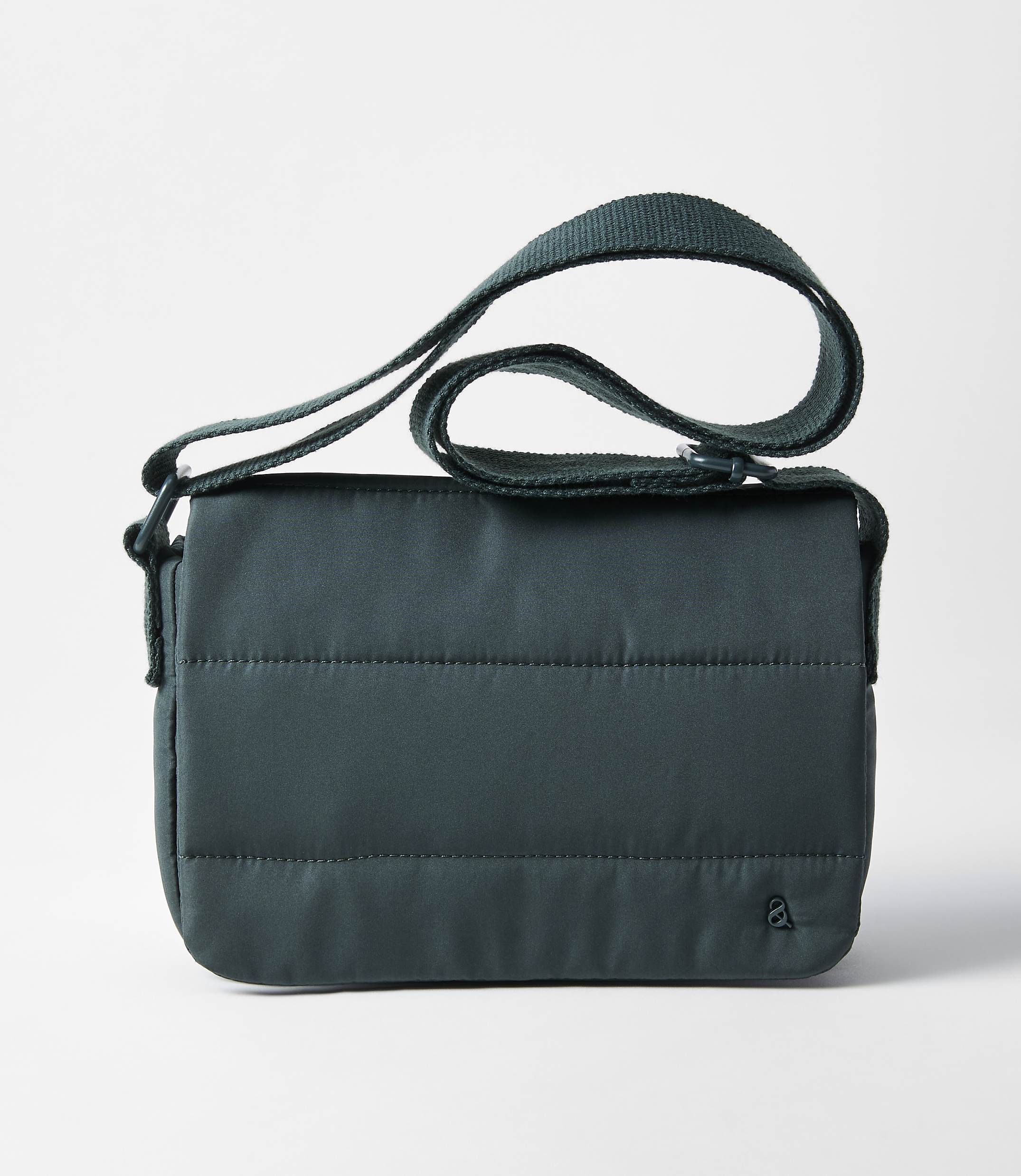 A dark teal quilted crossbody bag with a green strap rests on a plain white background.