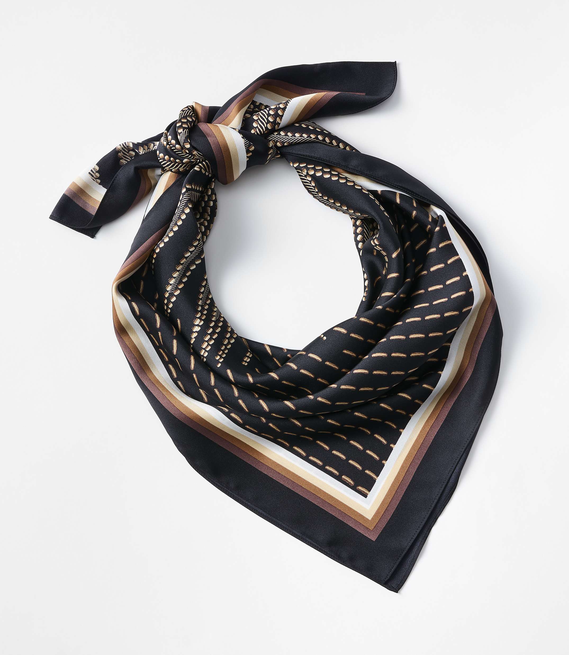 A black silk scarf with a geometric pattern of dots and lines in brown, beige, and white is tied in a knot against a plain white background.