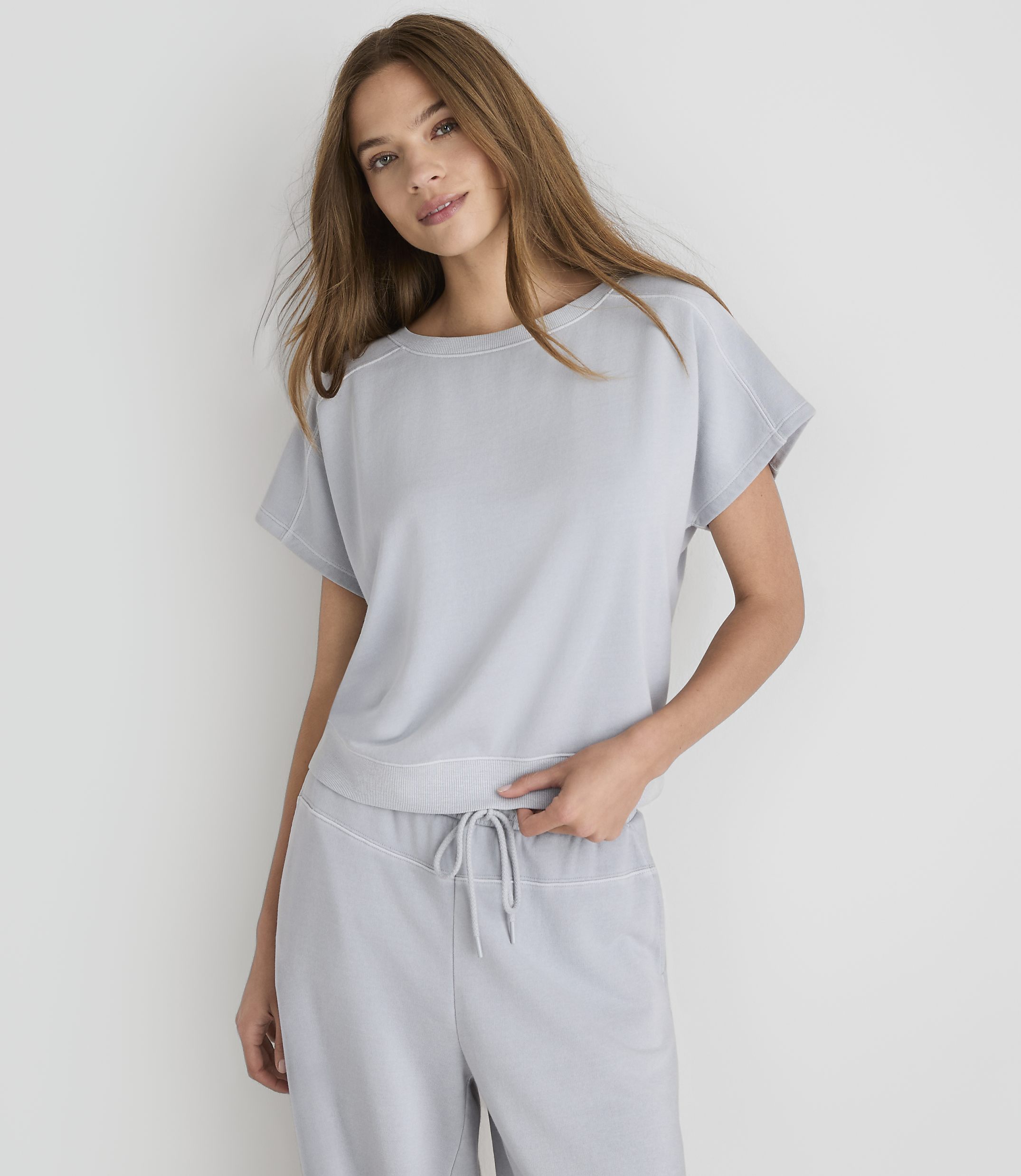 A woman in a light gray loungewear set stands against a plain white background.