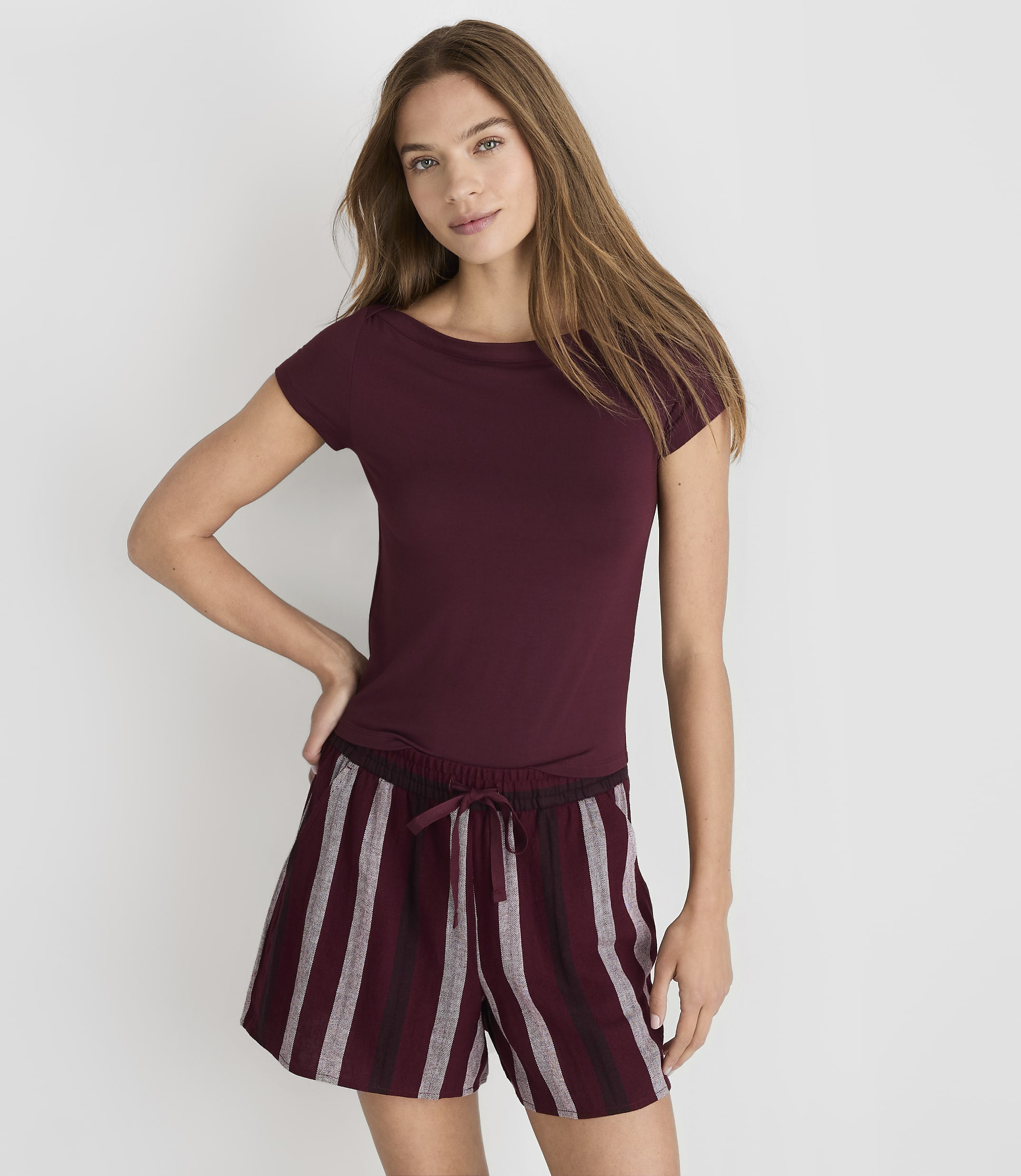 A woman in a maroon t-shirt and striped shorts stands against a plain white background.